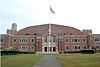 facade of the Teaneck Armory, with a green lawn, flagpole and tracked armored vehicles in front of the building.