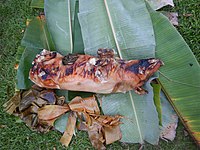 Photographie d'un cochon grillé présenté sur des feuilles de palmier.