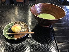 Bowl of macha green tea and small sweet on an oribe plate, at the Tōsui-an (陶翠庵) tea house at the Aichi Prefectural Ceramic Museum. The chawan is Ido type by Yamada Kazutoshi (山田和俊), the Oribe ware plate is from the ceramic craft studio of the museum done by staff.