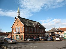 Vista de três quartos da Prefeitura de Easingwold com seus tijolos vermelhos com arcos amarelos e telhados inclinados de telhas cinza, quando o tempo está bom.