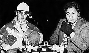 Photograph of two men seated at a table with drinks