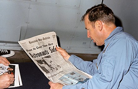Lovell reads a newspaper account of Apollo 13's safe return aboard recovery vessel USS Iwo Jima