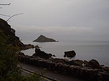 Foto tirada da costa onde uma pequena ilha rochosa aparece não muito longe.