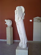 Statue de Niké (A245), de dos. Marbre de Paros, 480 - 470 av. J.-C. Au fond, torse d'hoplite (A756) (480 av. J.-C.) et stèle funéraire (milieu du Ve siècle av. J.-C.).