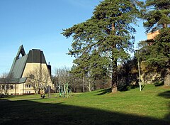 A southern view of the rear entrance to the church. In the foreground is playground equipment, a grass lawn and some trees.