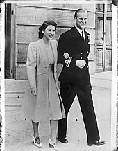 Photographie en noir et blanc d'un couple : la femme porte une robe claire, l'homme a un uniforme de couleur sombre.