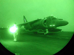 Mostly dark with green hue, this is a night-vision of jet aircraft getting ready for launch