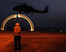 A long exposure of a United States Navy Landing Signalman Enlisted (LSE) directing a SH-60F Sea Hawk to take off using marshalling wands US Navy 110209-N-0864H-813 Culinary Specialist 3rd Class Drew Iverson directs an SH-60F Sea Hawk helicopter to take off from the U.S. 7th Fleet com.jpg