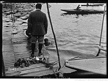 Photo en noir et blanc d'un sportif dans l'eau qui s'accroche à un ponton.