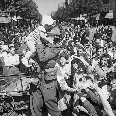 A British AFPU photographer kisses a child before cheering crowds in Paris, 26 August 1944.