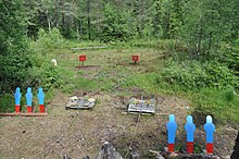 Steel targets down range at the stage. The shooter engages the targets with different weapons, using a rifle for the distant red targets, and revolvers for the closer blue targets. Cowboy Action Shooting - stage targets.JPG