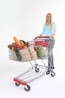 A shopping cart held by a woman, containing bags and food. Frau mit Einkaufswagen (37939692236).jpg