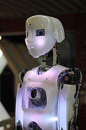 Hvid humanoid-robot i profil, belyst med et let lilla lys.