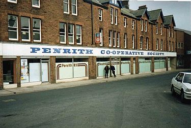 In the early 1990s, the society maintained a distinctive local identity, alongside the 1968 national Co-op cloverleaf visible in the windows of its Burrowgate premises Penrith Co-Op.jpg