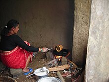 A woman cooking sel roti in a traditional Nepalese wooden stove