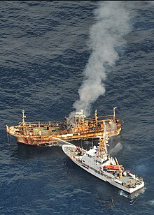 USCGC Anacapa directs streams of water into the Japanese derelict Ryou-Un Maru to sink it after shelling it. Holes from the Mk 38 25 mm chain gun is clearly visible on the bow of the cutter. 120405-G-RS249-005-USCG responds to Japanese vessel in Gulf of Alaska.jpg