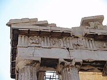 Bâtiment antique : haut des colonnes, entablement et toit. Décor sculpté en bas relief en haut et en arrière plan des colonnes cannelées