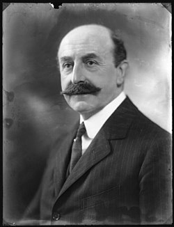 Monochrome portrait photograph of Sir Anderson Montague-Barlow. He is shown in three-quarter profile wearing a suit, white shirt, and tie. He has a large moustache and a bald pate.