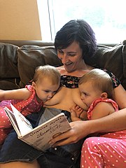 Woman breastfeeds 2 year old twins whilst reading them a book.
