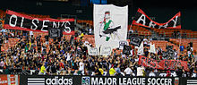 Болельщики в черном цвете с несколькими большими изображениями на трибунах стадиона.