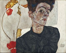 Portrait en plan poitrine d'un homme brun aux yeux marrons vêtu de noir, tête inclinée vers sa gauche, tiges de fleurs à sa droite