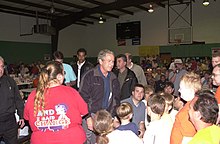 Photograph of a crowd of adults and children at a school gymnasium. George W. Bush is at the center of the image.