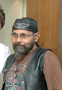 Un Indien barbu avec spectacle debout, souriant, une casquette noire autour de la tête