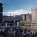 קנדי ומארחיו הגרמנים צופים מעל במה אל מעבר לחומת ברלין.