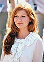 A red-headed woman smiles while wearing a white top with frill detailing