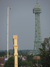 Een nauwelijks zichtbare figuur staat op een koord verbonden door een grote paal en een replica van de Eiffeltoren