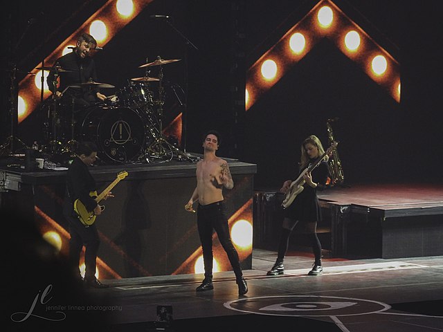 Panic! at the Disco at the Pepsi Center in 2018. From left to right: Kenneth Harris (guitar), Dan Pawlovich (drums), Brendon Urie (vocalist), and Nico