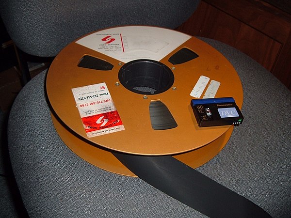 A 14-inch reel of 2-inch quad videotape compared with a modern-day MiniDV videocassette. Both media store one hour of color video.