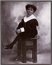 Photographie en noir et blanc d'un jeune garçon aux cheveux bouclés, assis, une jambe croisée sur l'autre, et vêtu d'un costume de marin.