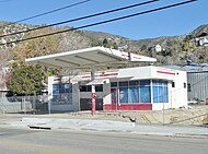 A white and red Texaco gas station, with a chainlink fence surrounding it. There is a road in front of the station.
