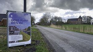 Ingang naar Huizinge met links een bord van de NAM met betrekking tot leefbaarheidsplannen voor door aardbevingen getroffen dorpen en rechts de Janskerk die ook beschadigd raakte bij de aardbeving