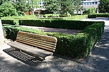 Celkový pohled do zahrady s lavičkou a do pozadí na živé ploty, kde jsou umístěny stěny termálních lázní