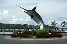 Sculpture d'un gros poisson sur un rond-point en bord de mer.