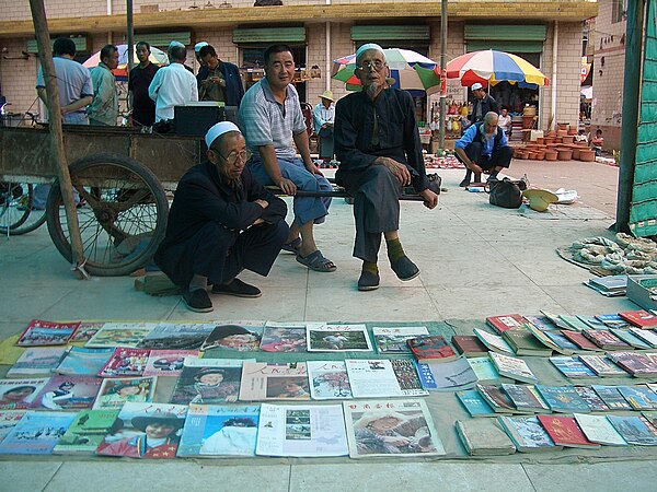 Two Hui book vendors at a Linxia City market, wearing traditional eyeglasses