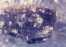 Small glassy lunar sample peppered with microcraters. The central pits are surrounded by bright spallation zones. LunarMicrocraters.jpg