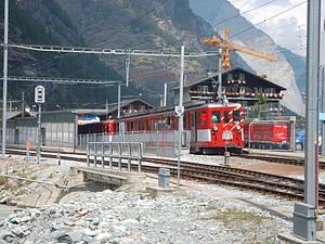 Rot-weißer Zug vor einem vierstöckigen Gebäude im Chaletstil mit Satteldach