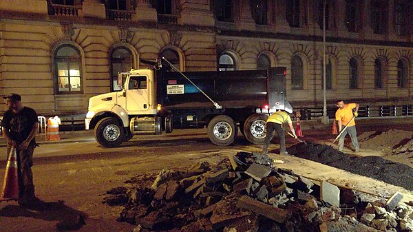 Construction crew laying down asphalt over fiber-optic trench, in New York City