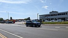 A Tesla Dealership building, cars are parked in front of the building and another car is passing by the building.