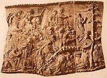 29th and 30th scenes from Trajan's Column. Infantry attack the Dacians, who flee while riders torch their settlement. Amidst the chaos, Trajan compassionately gestures to a woman holding her child Trajan's Column 29-30.jpg