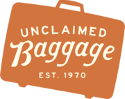 Siluet dari sebuah koper dengan teks "Unclaimed Baggage, Est. 1970"