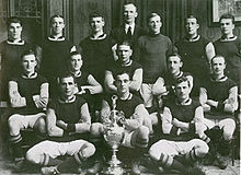 A black and white picture of a football team posing behind a football trophy