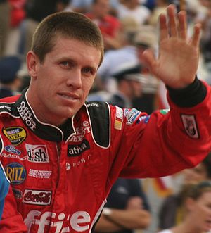 Edwards, with close cropped hair, waves while wearing his red, sponsor-filled racing suit.