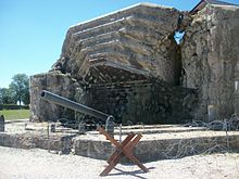 A heavily damaged concrete fortification with a protruding gun barrel.