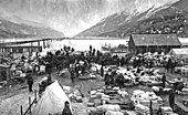 Första guldfyndet görs i Klondike denna dag för 127 år sedan, och utlöser den efterföljande guldruschen. Fotografiet visar ett guldgrävarläger i Dyea i Alaska under guldruschens dagar.