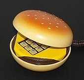 Photographie d’une forme de hamburger entrouvert laissant apparaître le clavier d’un téléphone jaune.