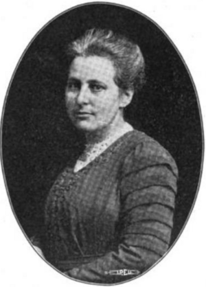 A photograph of a middle-aged white woman in an oval frame; she is wearing a dress with a distinctive pleating on the upper sleeve; her hair is dressed in an updo